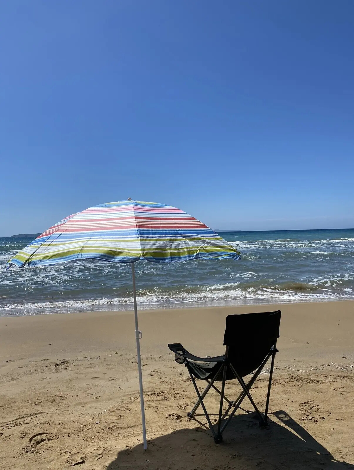Sonnenschirm und Stuhl an einem ruhigen Strand auf Korfu